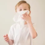 Bata na naka-white shirt na gumagamit ng wet wipes para linisin ang ilong.