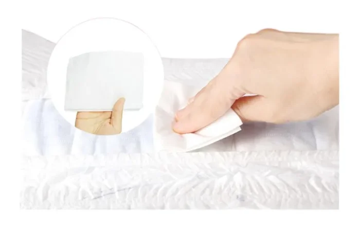 Kamay gamit ang puting wet wipe sa tela malapit sa ultra-wide waistband na mga lampin ng sanggol.