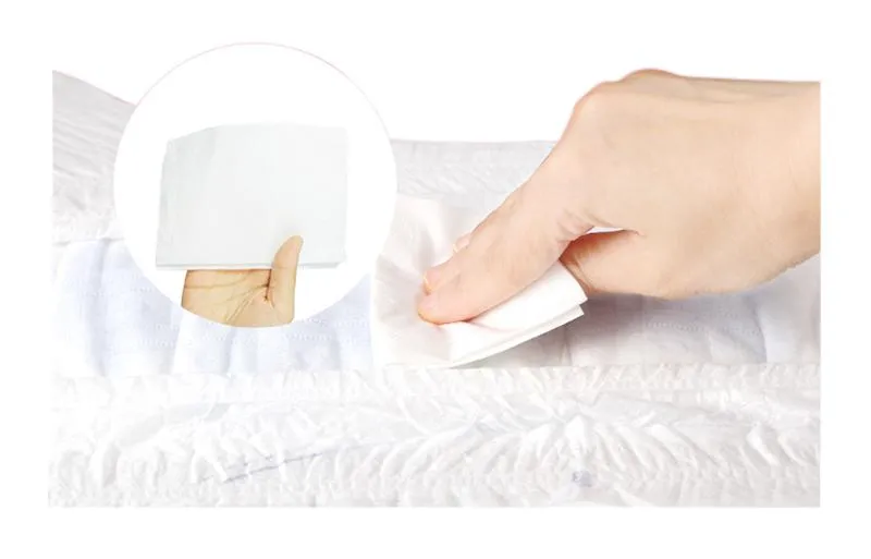 Kamay gamit ang puting wet wipe sa tela malapit sa ultra-wide waistband na mga lampin ng sanggol.