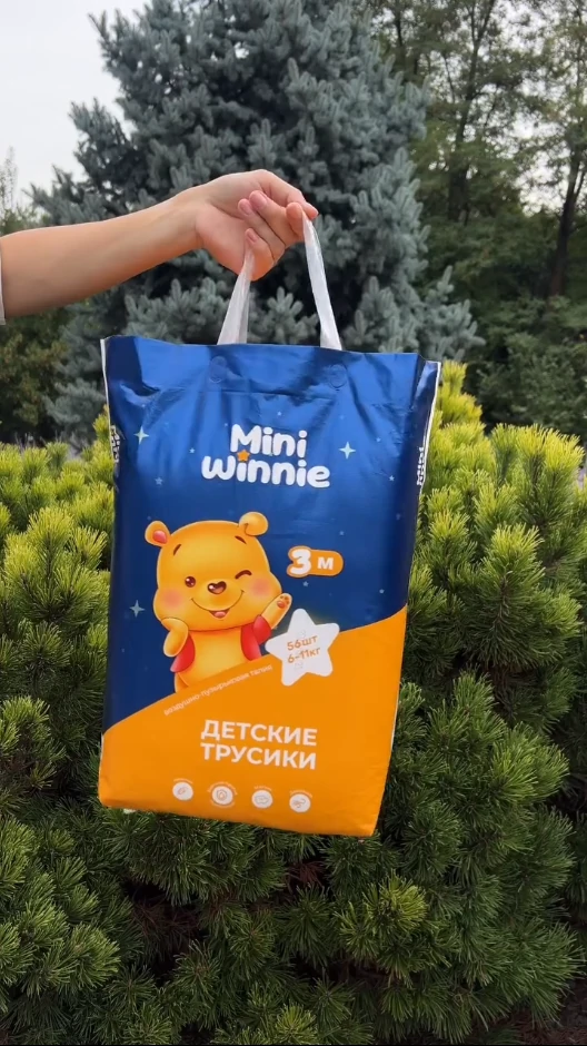 Kamay na may hawak na baby diaper pack na may disenyo ng oso, mga puno sa background.